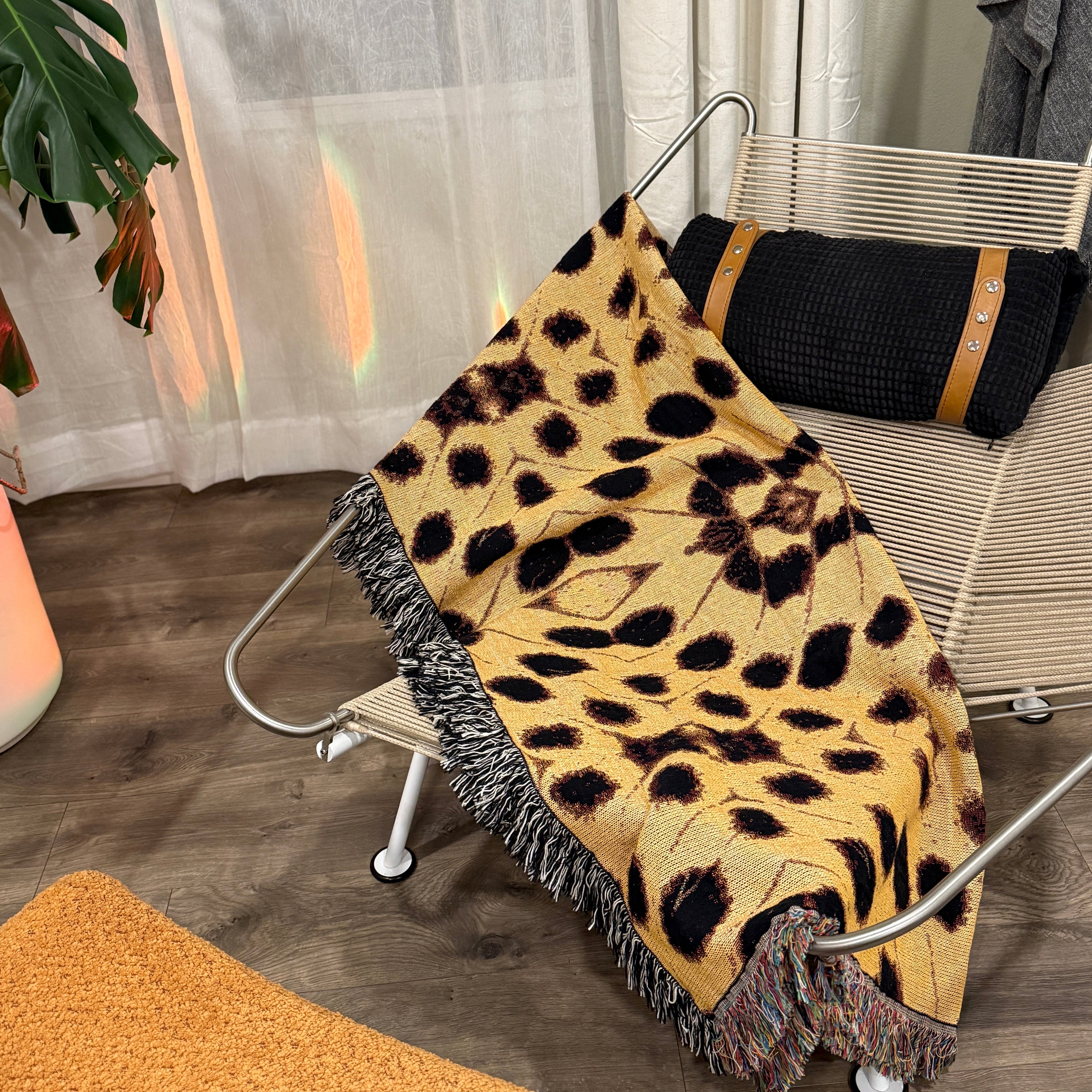 Leopard print blanket draped over a chair in a room with curtains and a plant.