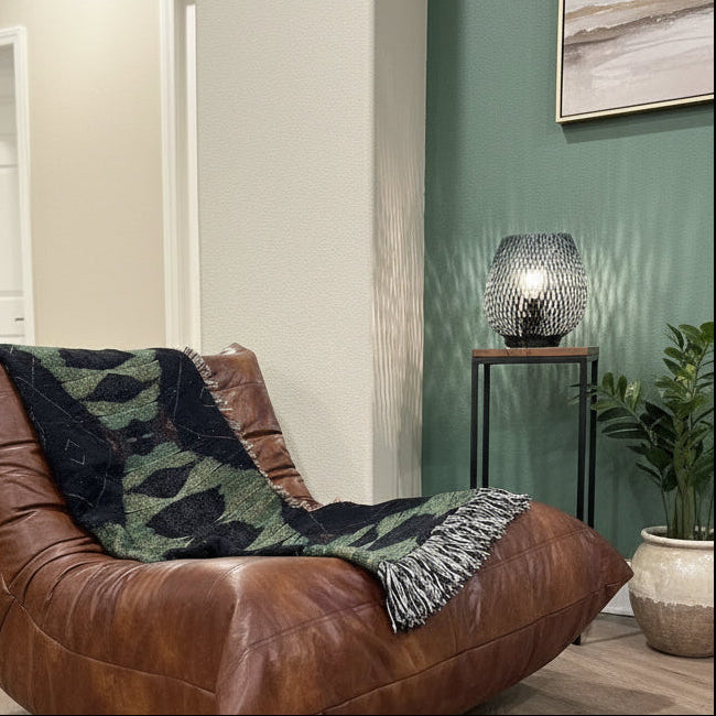Brown leather chair with a patterned blanket in a room with wooden flooring and a green wall.