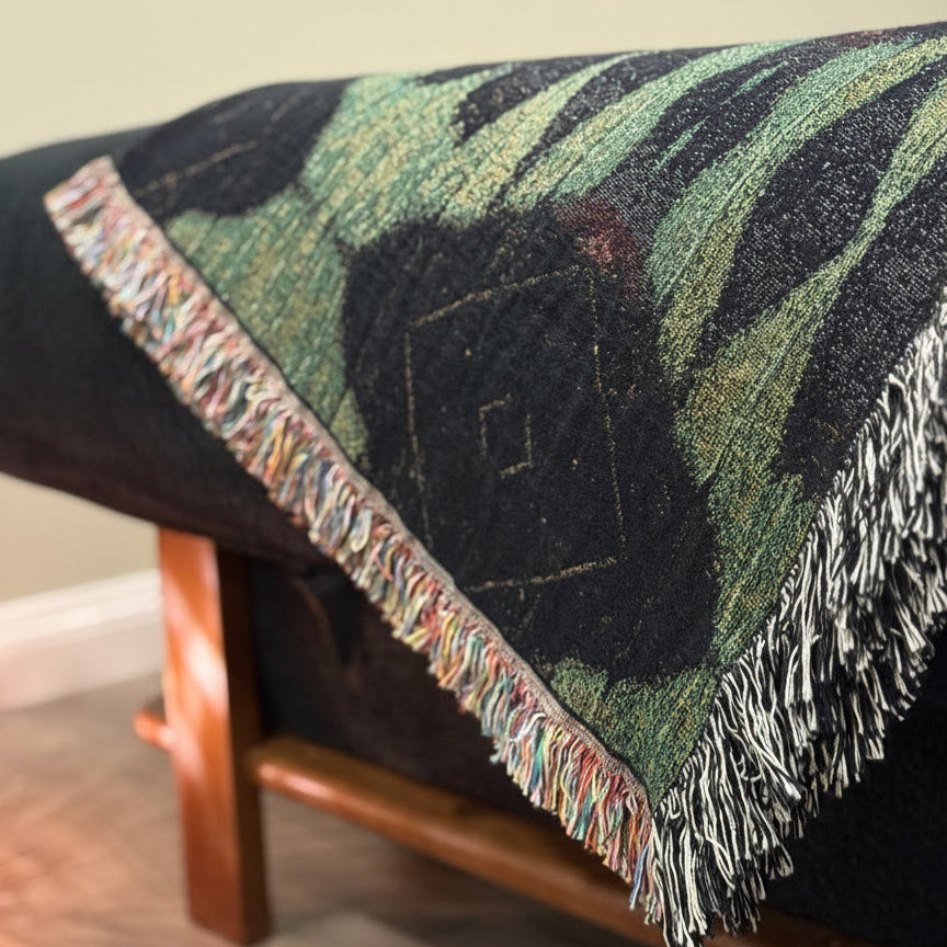 A green and black patterned throw blanket draped over a black sofa