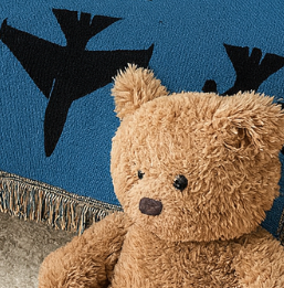 Children's room with a gray crib, blue blanket with black birds, and teddy bear.