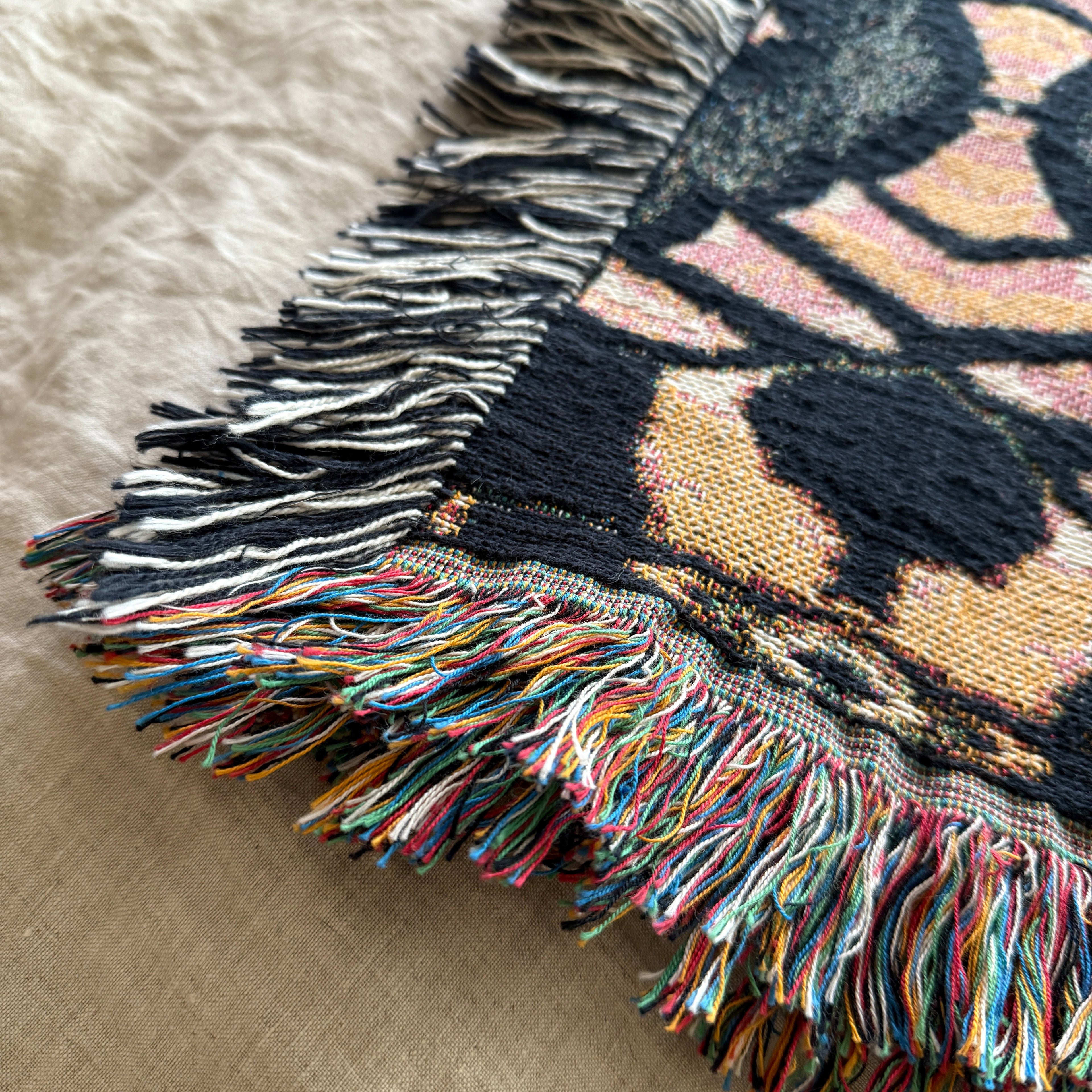 Close-up of a textured blanket with fringe on a beige surface