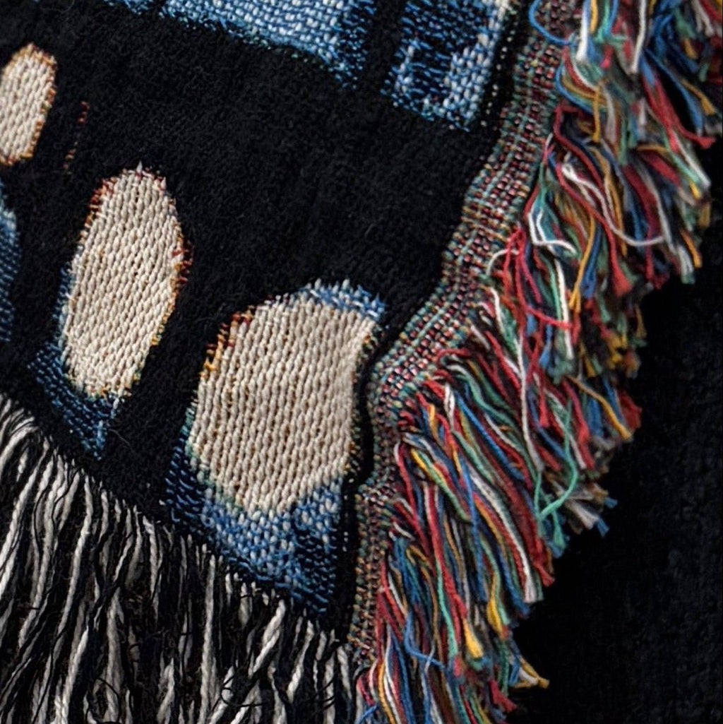 Textured throw blanket with fringe on a black surface, next to a lit candle.