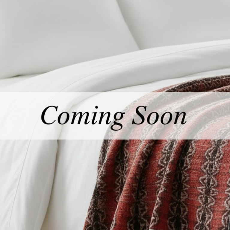 White bedding with a patterned throw blanket on a bed, featuring 'Coming Soon' text.