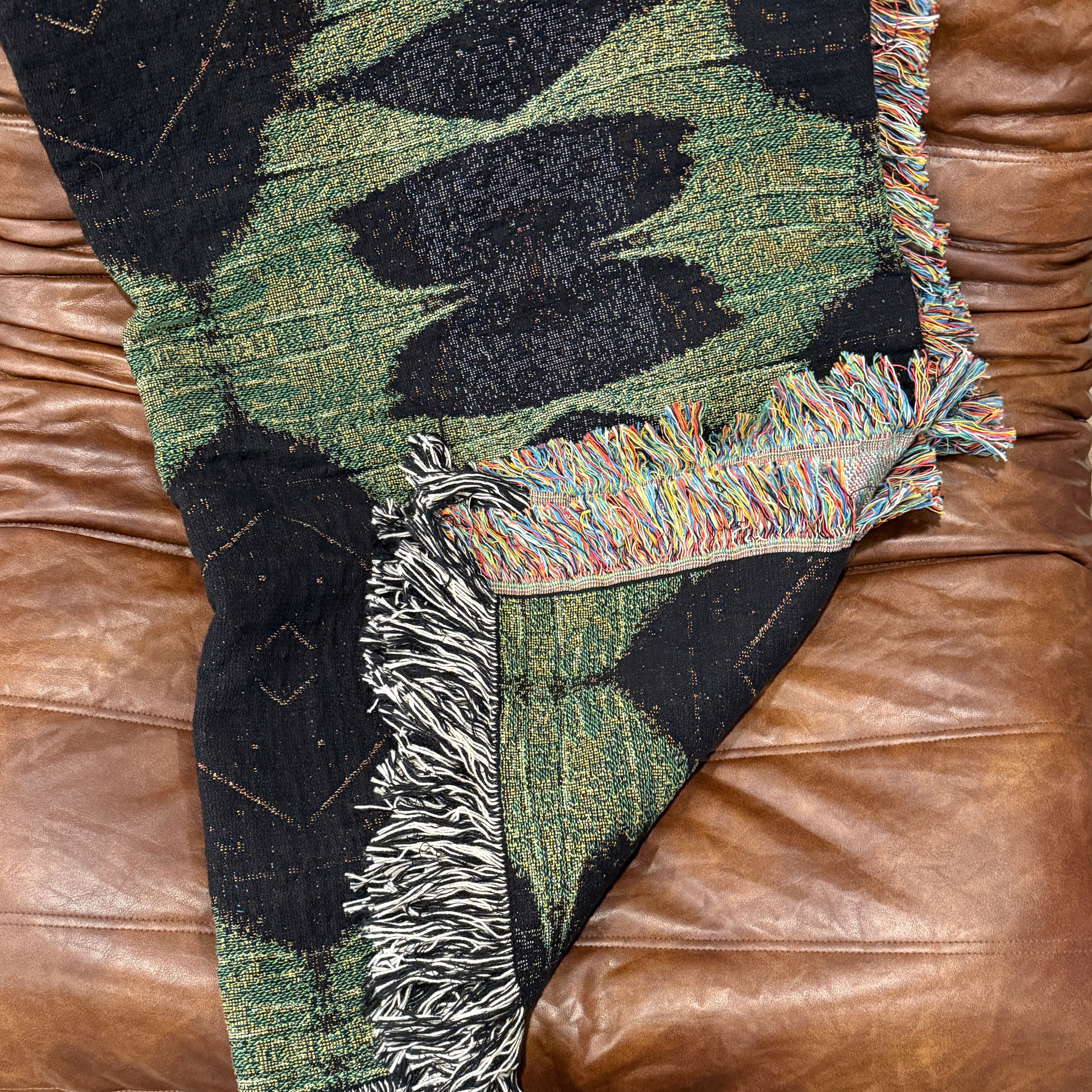 Camouflage-patterned blanket with fringes draped over a brown leather couch.